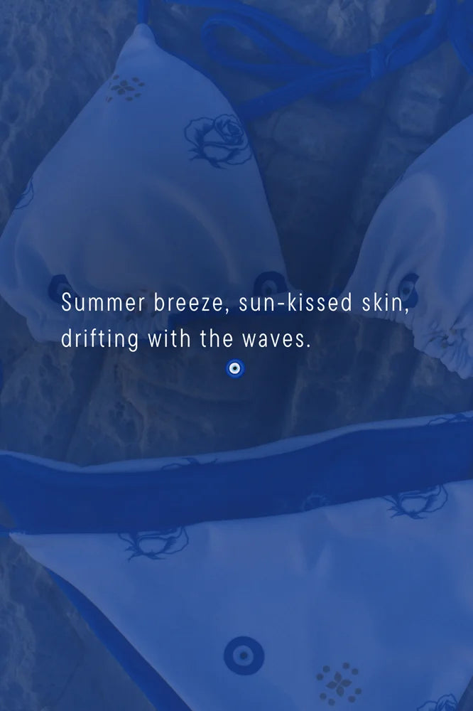 Woman wearing a blue and white bikini set with a scenic background of water and rocks. greece swimsuit resort aesthetic vacation swimwear aegean 
White Greek Evil Eye triangle bikini set with blue straps, gold sunburst motifs, and tie-side cheeky bottoms. Hand-drawn Mediterranean inspired design.