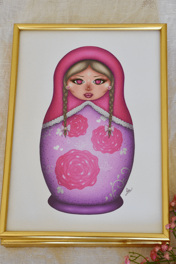 Framed artwork of a pink matryoshka doll with floral patterns on a light background.